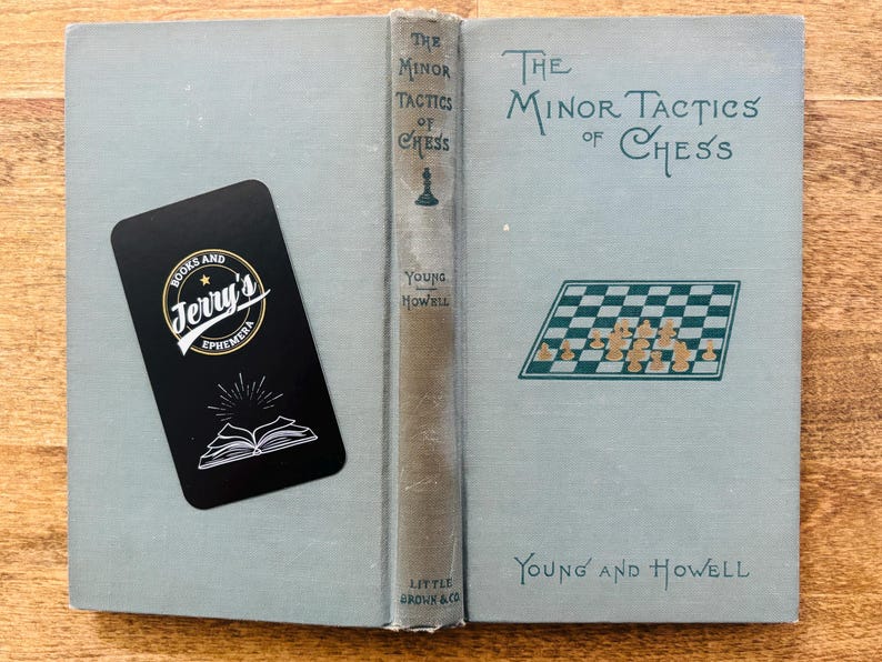 May include: Open book titled "The Minor Tactics of Chess" with a light blue cover and a chess board illustration. A black bookmark with "Jerry's Ephemera" logo is on the left. The book is by Young and Howell.