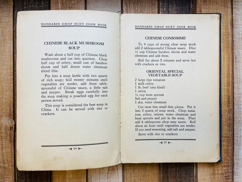 Pu&ograve; includere: Pagine di un libro di cucina aperto con ricette di zuppe cinesi. La pagina sinistra presenta la Zuppa di Funghi Neri Cinese, mentre la destra offre Consomm&eacute; Cinese e Zuppa di Verdure Speciale Orientale. Su una superficie di legno.