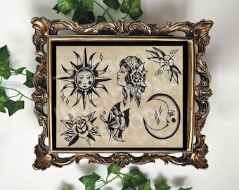 May include: A framed print featuring traditional tattoo designs. The black and white illustrations include a sun with a face, a woman's profile, a rose, a butterfly, a crescent moon, and floral elements. The frame is ornate and gold-colored.
