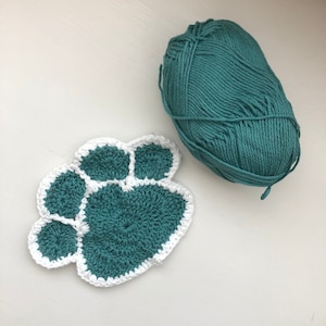 May include: A teal crocheted paw print with a white border, next to a ball of teal yarn.