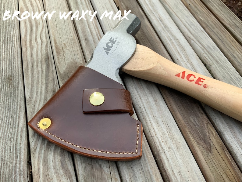 Pu&ograve; includere: Un'ascia con manico in legno e testa in metallo, parzialmente coperta da un fodero in pelle marrone. La testa dell'ascia &egrave; stampata con "ACE" e "1-1/2 LB". Il testo "BROWN WAXY MAX" &egrave; nella parte superiore dell'immagine.