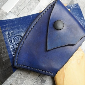 May include: A blue leather axe sheath with a black button closure. The sheath is made of thick, durable leather and has a stitched edge.