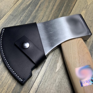 May include: A black leather axe sheath with a white stitch detail and a silver snap closure. The sheath is attached to a wooden axe handle with a silver axe head.
