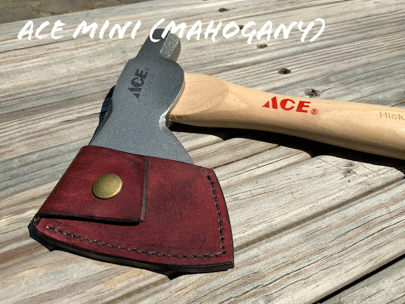 Pu&ograve; includere: Ascia con testa argentata e manico in legno, con la scritta "ACE" in rosso. L'ascia &egrave; parzialmente coperta da un fodero in pelle bordeaux con chiusura a bottone in ottone. Il testo "ACE MINI (MAHOGANY)" &egrave; in alto.