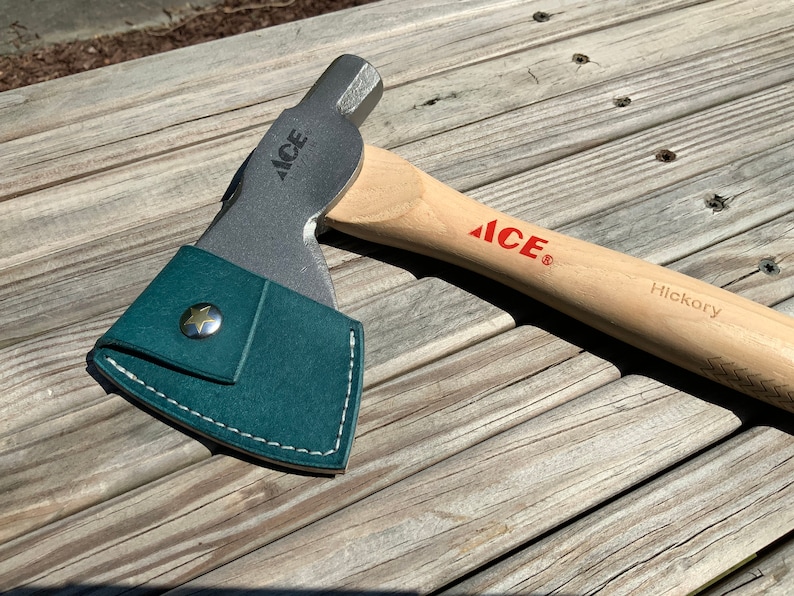 Pu&ograve; includere: Un'ascia con manico in legno e testa in metallo, con il logo "ACE" in rosso. La testa dell'ascia &egrave; parzialmente coperta da un fodero in pelle verde acqua con un bottone a forma di stella. Il manico &egrave; etichettato "Hickory".