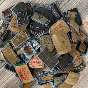 Könnte beinhalten: Ein Haufen verschiedener Denim-Patches, viele mit Lederetiketten. Die Etiketten zeigen Texte von Marken wie Levi Strauss, Lee und anderen. Die Patches sind in verschiedenen Blau-, Braun- und Beigetönen gehalten und weisen sichtbare Nähte und Abnutzung auf.