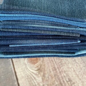 May include: A stack of denim fabric in various shades of blue. The fabric is folded neatly and appears to be new.