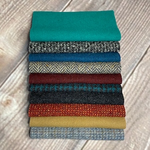 Pode incluir: Um conjunto de 10 amostras de tecido de diferentes cores e padrões, incluindo turquesa, cinza, azul, bege, vermelho, preto e laranja. As amostras estão dispostas em uma pilha vertical, com a amostra turquesa na parte superior e a amostra cinza na parte inferior.