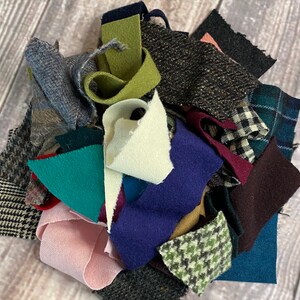 K&ouml;nnte beinhalten: Eine Sammlung von Stoffresten in verschiedenen Farben und Texturen. Enth&auml;lt St&uuml;cke aus Tweed, Wolle und anderen Materialien in Blau-, Gr&uuml;n-, Rosa- und Graut&ouml;nen. Einige St&uuml;cke weisen Muster wie Karos und Hahnentritt auf.