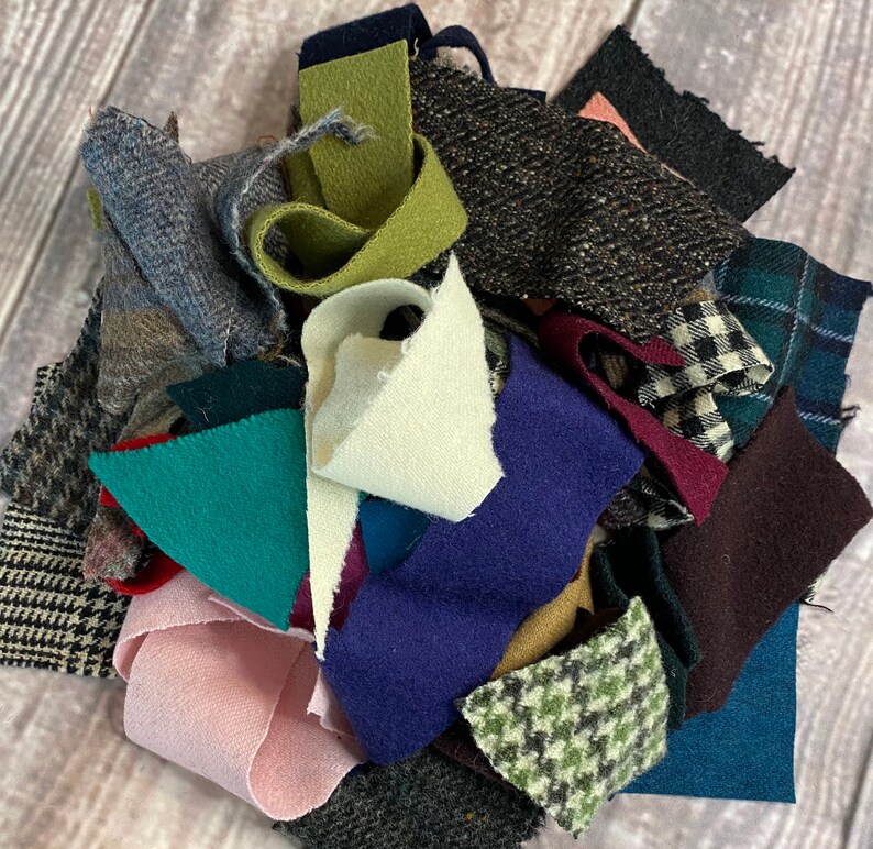 K&ouml;nnte beinhalten: Eine Sammlung von Stoffresten in verschiedenen Farben und Texturen. Enth&auml;lt St&uuml;cke aus Tweed, Wolle und anderen Materialien in Blau-, Gr&uuml;n-, Rosa- und Graut&ouml;nen. Einige St&uuml;cke weisen Muster wie Karos und Hahnentritt auf.