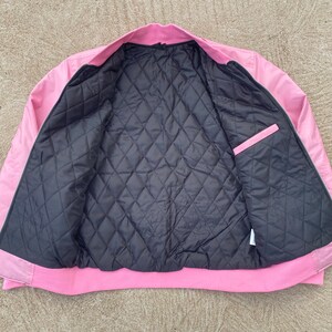 May include: A pink satin bomber jacket with a black quilted lining. The jacket has a zipper closure and two pockets.