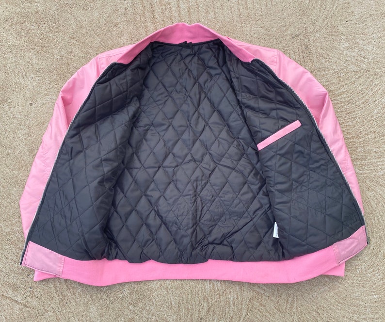 May include: A pink satin bomber jacket with a black quilted lining. The jacket has a zipper closure and two pockets.