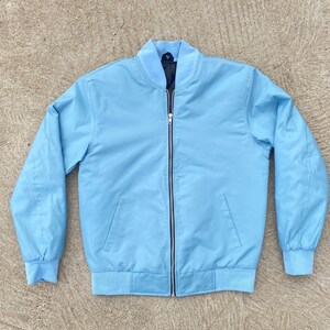 May include: A light blue bomber jacket with a zipper closure. The jacket has a ribbed collar, cuffs, and hem.