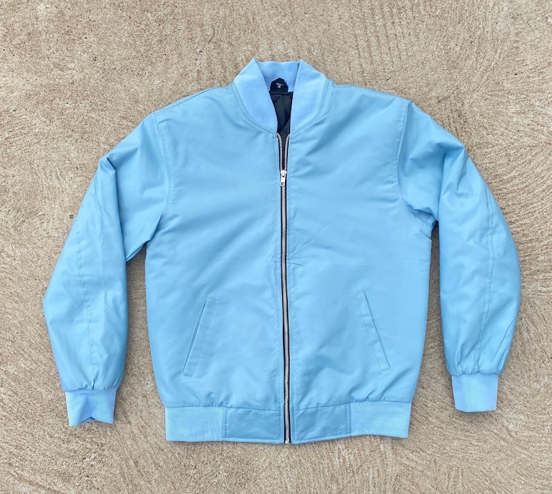 May include: A light blue bomber jacket with a zipper closure. The jacket has a ribbed collar, cuffs, and hem.