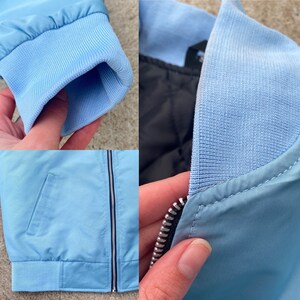 May include: A light blue bomber jacket with a zipper closure and a ribbed collar. The jacket has a pocket on the left side and a silver zipper.
