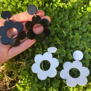 May include: A pair of black and white flower-shaped earrings. The black earrings have a large, round, open center. The white earrings have a large, round, open center.