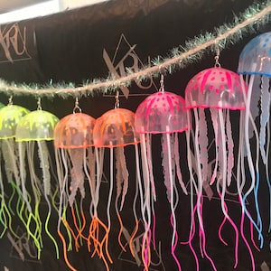 May include: A string of colorful jellyfish earrings. Each earring features a clear plastic jellyfish with a neon colored body and tentacles.