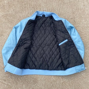 May include: A light blue bomber jacket with a black quilted lining. The jacket has a zipper closure and two pockets.