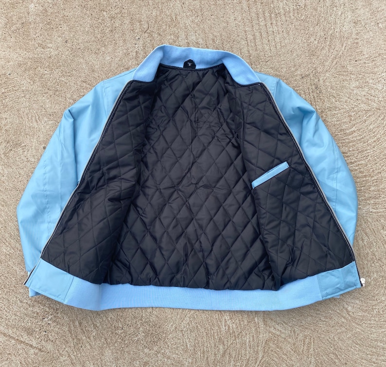 May include: A light blue bomber jacket with a black quilted lining. The jacket has a zipper closure and two pockets.