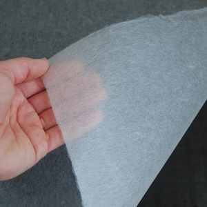 May include: A close-up of a white, textured sheet of paper being lifted from a dark grey surface. The paper is thin and translucent, revealing the surface beneath.