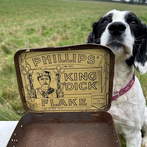 May include: A vintage metal tobacco tin with a rusty exterior. The lid features a yellow label with the text "Phillips' King Dick Flake" and a drawing of a man in a crown. The text "Registered Trade Mark No. 297597" is also on the label.