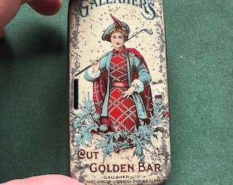 Könnte beinhalten: Vintage rechteckige Tabakdose aus Metall mit einem Bild einer Frau in schottischer Tracht, die einen Golfschläger hält. Der Text lautet "Gallaher's Cut Golden Bar" und der Firmenname. Dose hat ein gealtertes Aussehen.