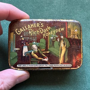 May include: A rectangular tin with a vintage illustration. The tin features the text "Gallaher's Rich Dark Honeydew" and a scene of people in a room. The bottom of the tin reads "THIS LABEL IS REGISTERED UNDER THE TRADE MARKS ACT NO 91584."