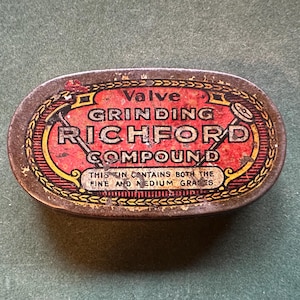 May include: A round, metal tin with a red, yellow and gold label. The label reads "Valve Grinding Richford Compound" and "This tin contains both the fine and medium grades".