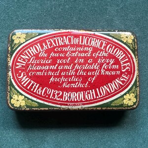 May include: A rectangular vintage tin with a red and white oval label, featuring the text "MENTHOL & EXTRACT OF LICORICE GLOBULES." The tin has a green border with yellow floral accents and the text "SMITH & CO 132, BOROUGH, LONDON, S.E."