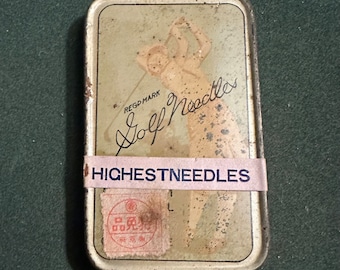 Könnte beinhalten: Eine Vintage-Blechdose mit einem Golfer-Bild und dem Text "Golf Needles" und "HIGHEST NEEDLES". Die Dose hat einen roten Stempel mit japanischen Schriftzeichen.