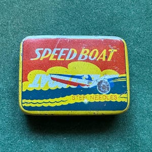 May include: Rectangular tin with a red top and yellow border. The words "SPEED BOAT" are printed across the top. Below the text is a graphic of a speed boat on blue water. The bottom of the tin reads "STEEL NEEDLES".