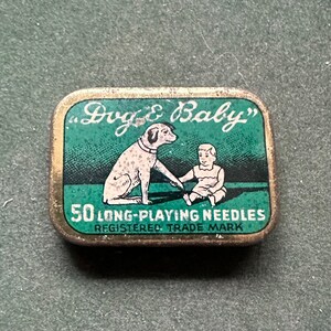 May include: A green and gold tin with the words "Dog & Baby" and "50 Long-Playing Needles" printed on it. The tin features a cartoon image of a dog and a baby playing together.
