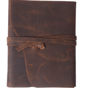 May include: A brown leather journal with a strap closure. The journal has a distressed look and is tied with a brown leather strap.