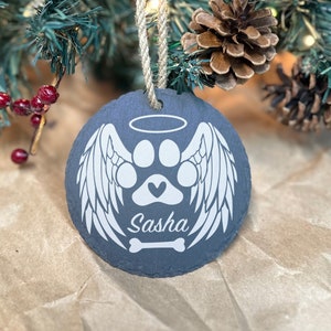 May include: A black slate Christmas bauble featuring a white paw print, wings, halo, and bone. The name "Sasha" is written beneath the paw print.