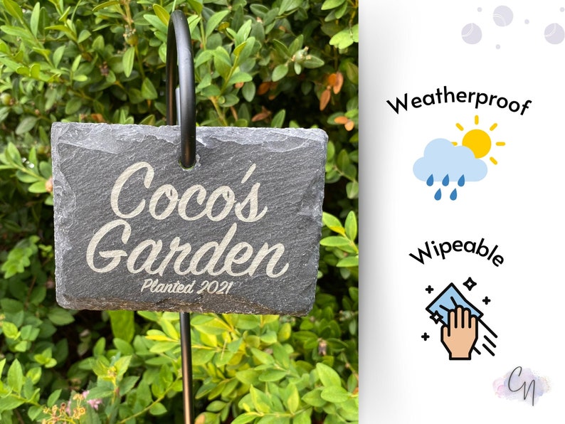 "Engraved 'Coco's Garden, Planted 2021' slate sign on metal stake amid vibrant green shrubs."