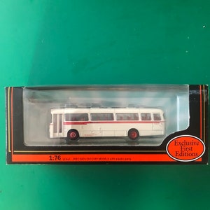 May include: A 1:76 scale model bus in a clear plastic case. The bus is white with a red stripe and red wheels. The packaging features the text "Exclusive First Editions". The model is a precision die-cast model.