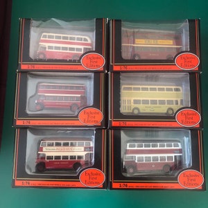 May include: Six boxed 1:76 scale die-cast model buses, featuring a variety of colors such as red, cream, and maroon. Each model is presented in a black box with orange detailing and is labelled "Exclusive First Editions".