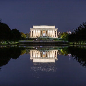 May include: A night view of the Lincoln Memorial in Washington, D.C., illuminated with lights. The memorial is reflected in the still water of the reflecting pool.