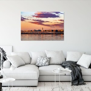 K&ouml;nnte beinhalten: Panoramablick auf eine Skyline bei Sonnenuntergang mit einem rosa und orangefarbenen Himmel und einem Gew&auml;sser im Vordergrund.