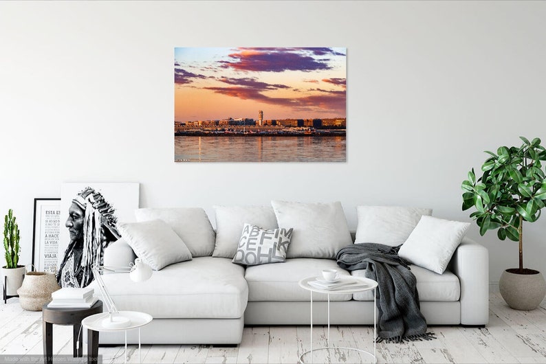 K&ouml;nnte beinhalten: Panoramablick auf eine Skyline bei Sonnenuntergang mit einem rosa und orangefarbenen Himmel und einem Gew&auml;sser im Vordergrund.