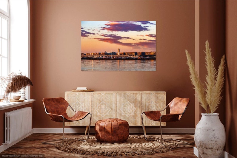 K&ouml;nnte beinhalten: Ein Wohnzimmer-Interieur mit zwei braunen Ledersesseln, einem Schrank aus Holz mit kunstvollen Schnitzereien, einem braunen Lederhocker und einem beigefarbenen Teppich. Ein gro&szlig;es Bild einer Skyline einer Stadt bei Sonnenuntergang h&auml;ngt an der Wand.