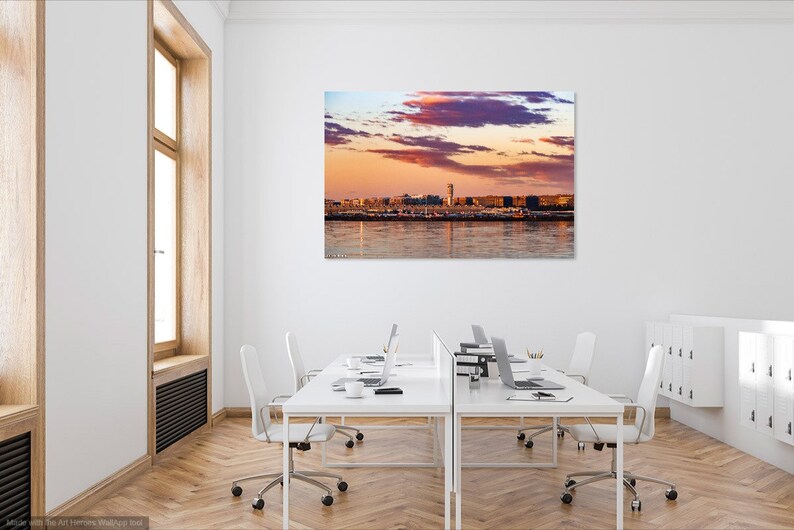 K&ouml;nnte beinhalten: Ein Panoramafoto einer Skyline bei Sonnenuntergang. Der Himmel ist ein lebendiges Gemisch aus rosa, lila und orangefarbenen Farbt&ouml;nen mit flauschigen Wolken. Die Stadt ist vor dem farbenfrohen Himmel silhouettiert, mit einem hohen Geb&auml;ude in der Mitte.