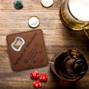 May include: A brown leather bottle opener with a metal opener and a printed design that says "Artifact of Unlocking" with a list of stats and a weight of 3.2. There are red dice with white numbers on a wooden surface.