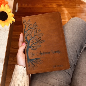 May include: A brown leather journal with a tree design and the text "The Anderson Family Est. 09.30.23" engraved on the front cover.