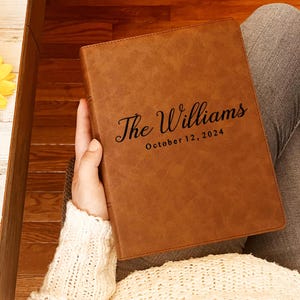 Könnte beinhalten: Ein braunes, ledergebundenes Tagebuch mit dem Text "The Williams October 12, 2024" auf der Vorderseite.