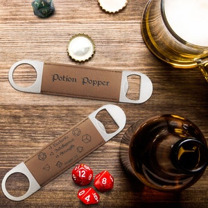 May include: Two brown and silver bottle openers, one with "Potion Popper" and the other with "+1 Dexterity, +2 Intelligence, +1 Strength". The image includes a beer glass, a bottle, dice, and bottle caps on a wooden surface.