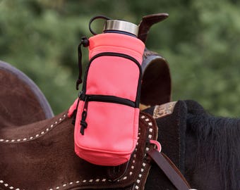 May include: A bright pink water bottle holder with a black zipper and drawstring is attached to a brown leather saddle. The holder has a black zipper pocket and a silver-colored bottle cap. The background is a blurred green.