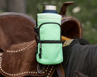 May include: A light green water bottle holder with a black zipper and drawstring is attached to a brown leather saddle. The holder has a pocket and holds a blue and silver water bottle. The saddle is on a horse.