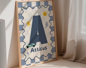 May include: A framed art print with the letter 'A' in blue, and the name 'Atticus' below. The background has a light blue and cream checkered pattern, with a star, lightning bolt, and a smiling sun. The frame is made of light wood.