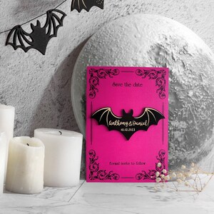 May include: A pink save the date card with a black bat silhouette and the text "Save the date" and "Anthony & Daniel 10.13.2023".